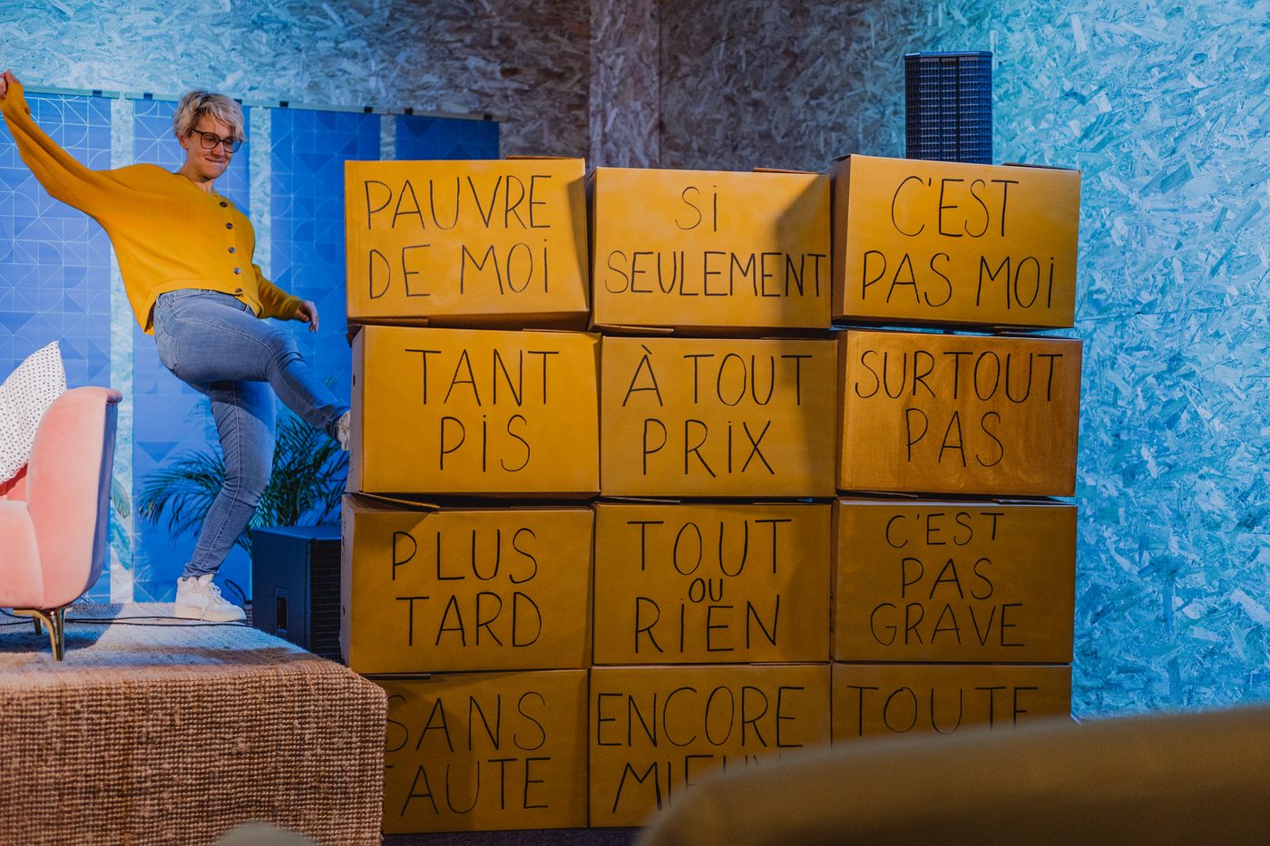 Hélène, sur scène, envoie valser du pied un mur de cartons portant des pensées toxiques : « pauvre de moi », « tant pis », « plus tard », « tout ou rien »