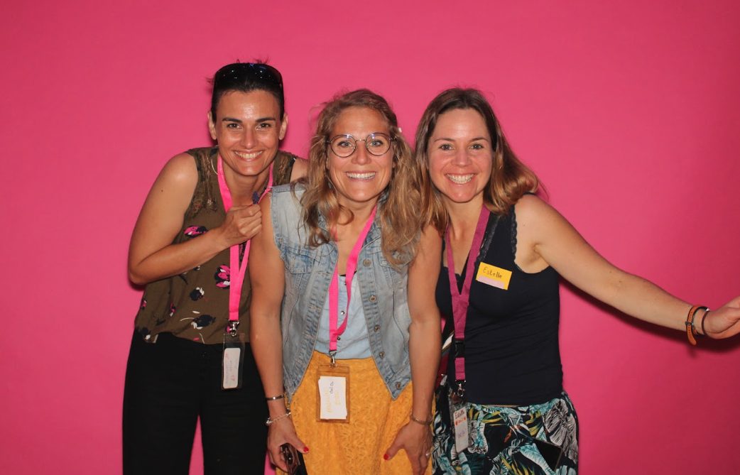 Trois Villageoises devant le fond rose du photomaton, badge autour du cou